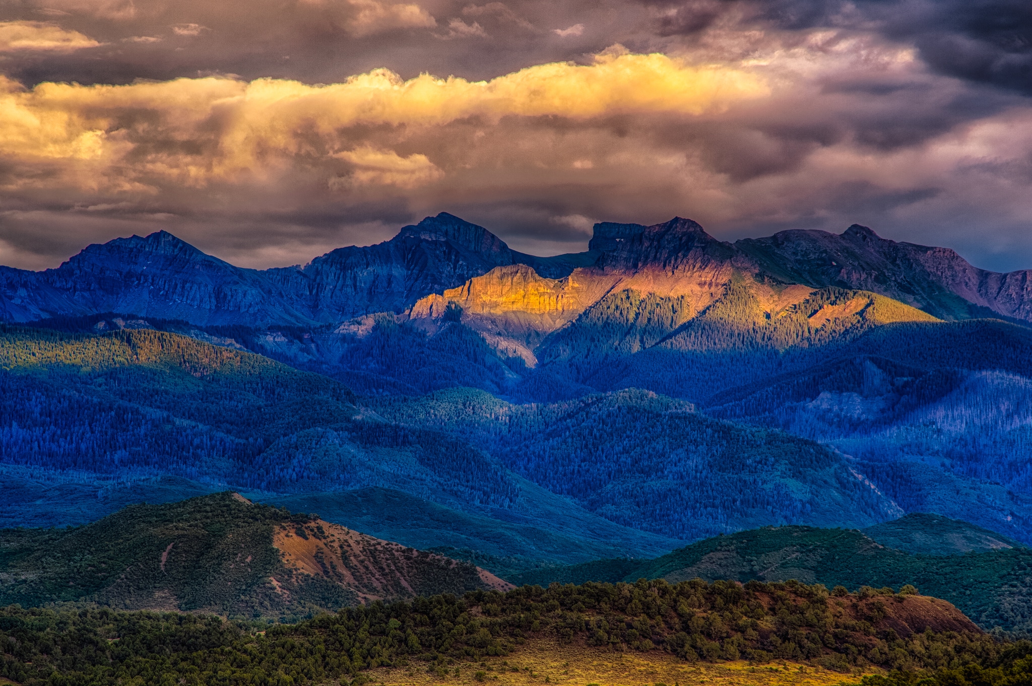 Late afternoon light escapes the heavy cloud cover to illuminate a portion of the Cimarron Mountains. Taken from Ridgway State Park near Ridgway, Colorado.