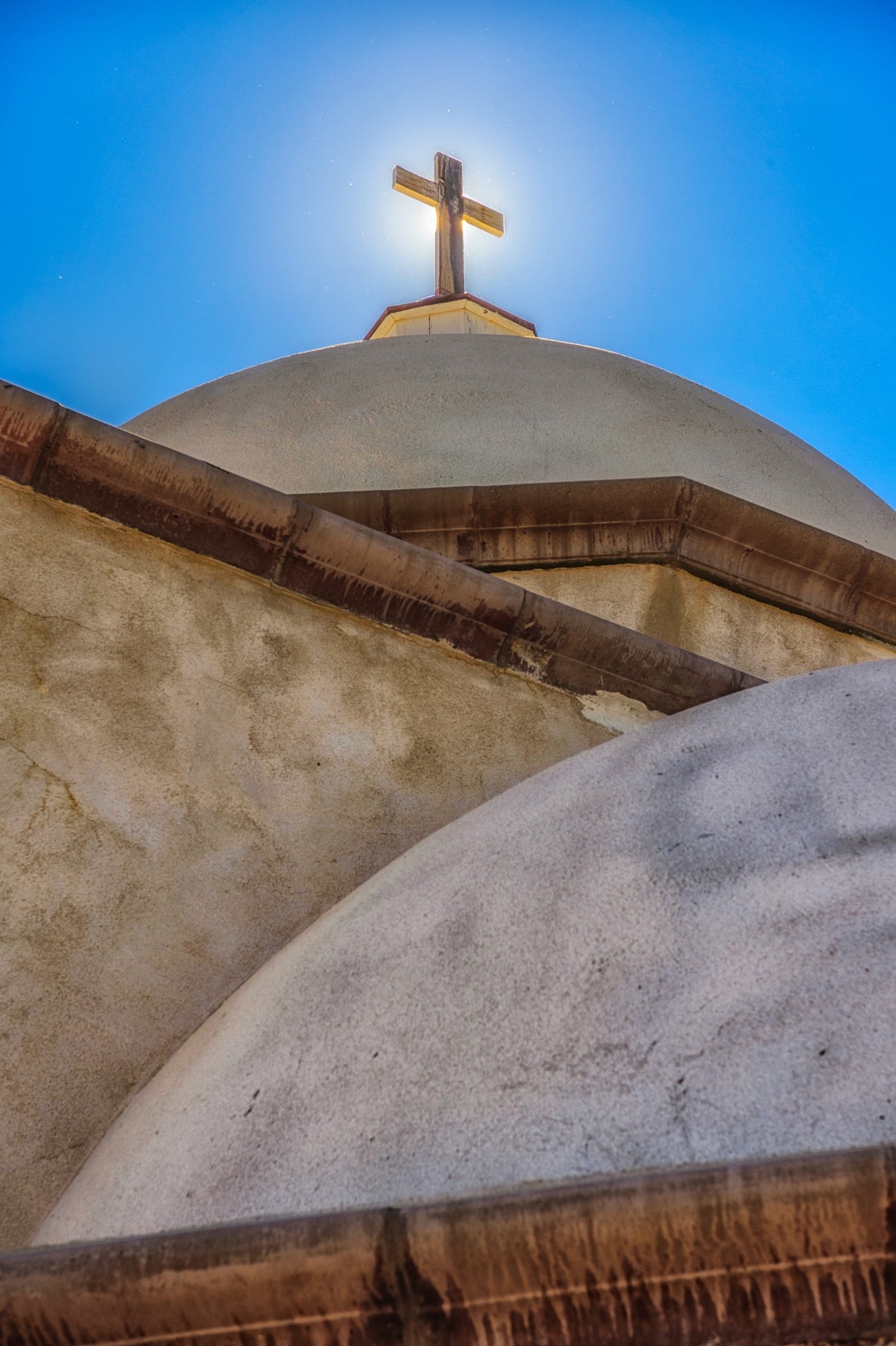 The sun silhouettes the wooden cross on top of the dome of La Capilla de Todos Los Santos, located above San Luis, Colorado, on La Mesa de la Piedad y de la Misericordia.