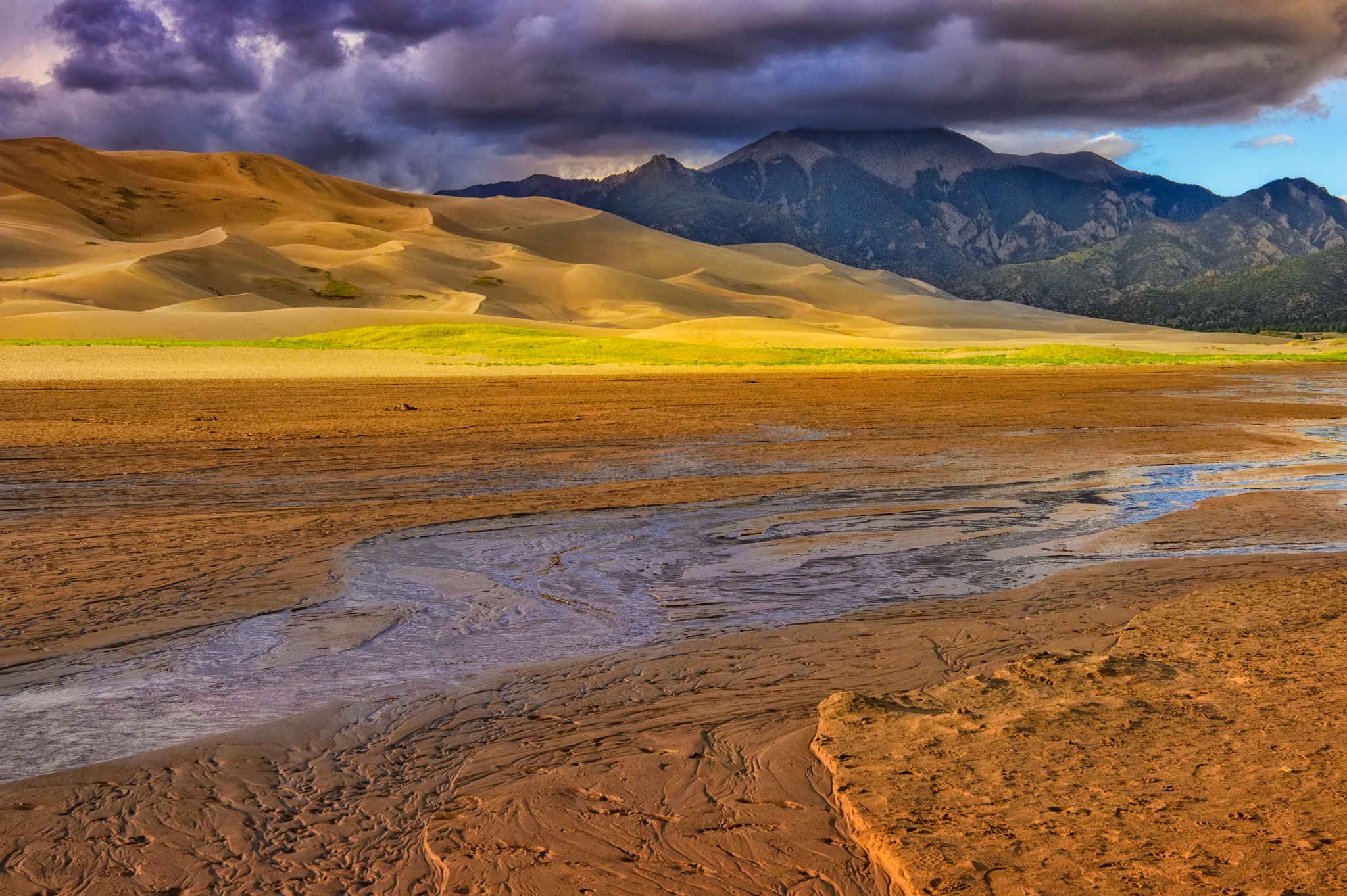 Golden afternoon light manages to sneak under the looming cloud cover of a retreating storm in Great Sand Dunes National Park and Preserve near Alamosa, Colorado.