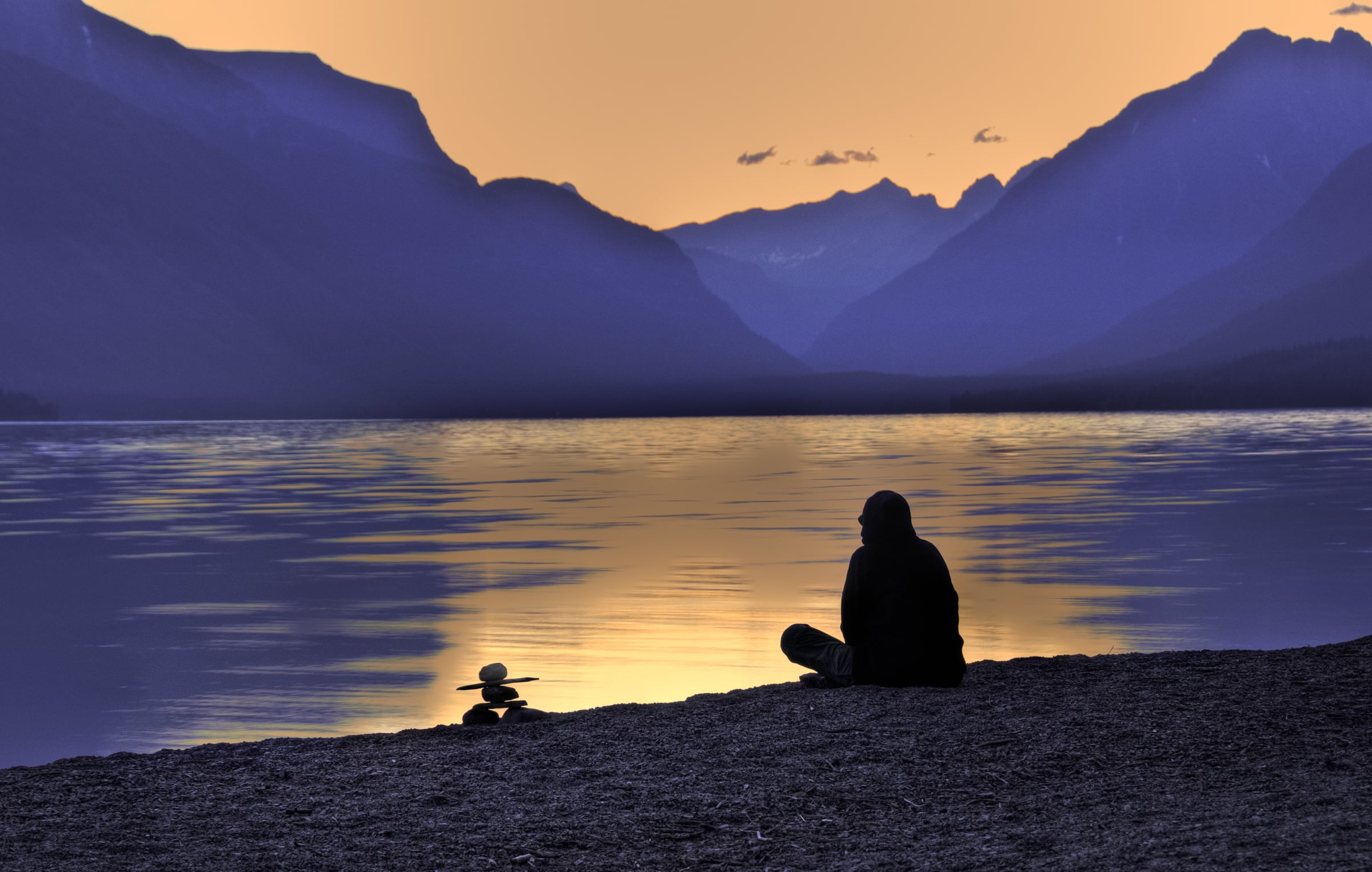 An early-morning hiker sits on a pebble beach on Lake McDonald awaiting dawn in Glacier National Park, Montana.
