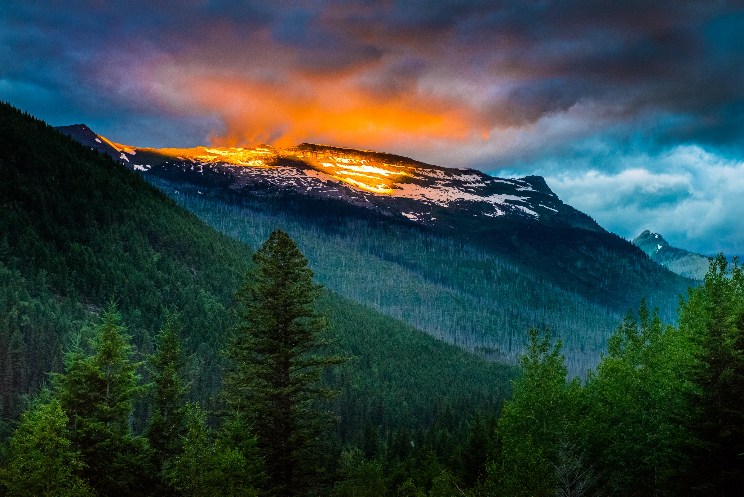 The rising sun breaks through the looming storm clouds to light up the snow atop Logan Pass in Glacier National Park in Montana.
