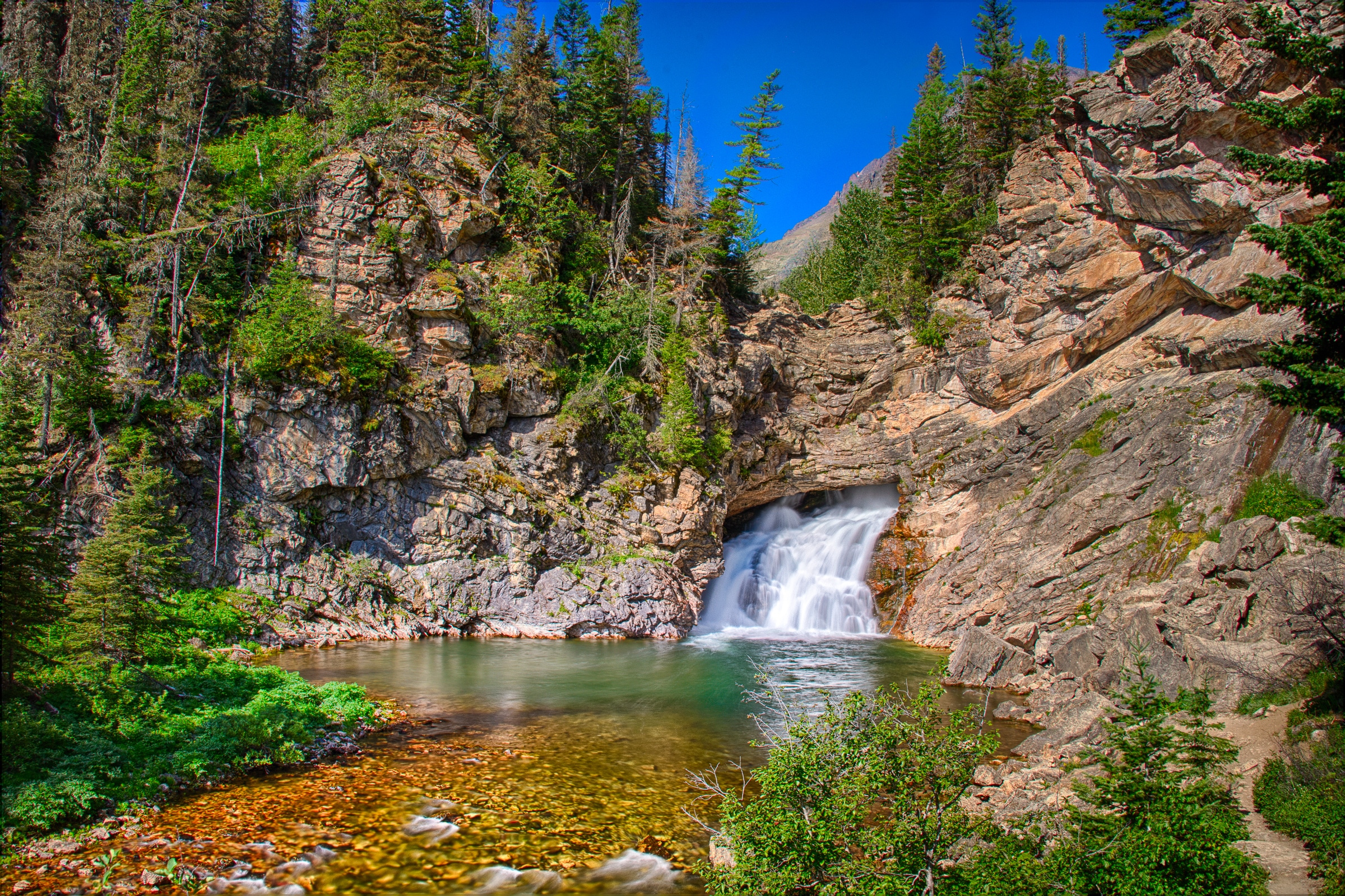 In late July, Running Eagle Falls, also known as Trick Falls, is flowing out of the lower opening. It is located near Two Medicine Trail in Glacier National Park, Montana.