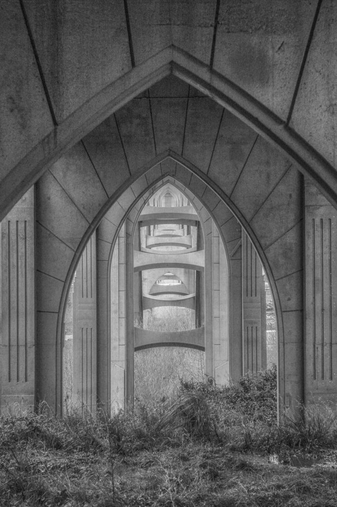 This black-and-white photo of the McCullough Memorial Bridge in North Bend, Oregon, is a view from beneath the approach span looking through the supporting concrete arches.