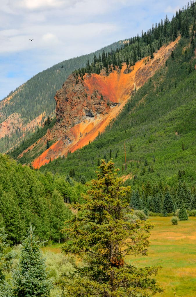 Viewed from US 550 heading north into Silverton, Colorado, this highly oxidized and mineralized volcanic intrusion stands out against the deep green of the surrounding spruce forest. It is on the western slope of Anvil Mountain and is part of the western edge of the Silverton Caldera, which formed over 30 million years ago.