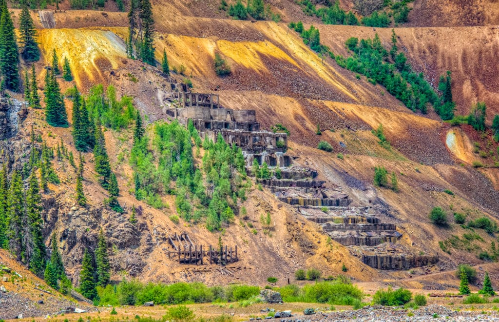 Taken from San Juan County Road 2 along the Animas River near Eureka Gulch, is a close-up view of the ruins of the Sunnyside stamping mill against a background of highly oxidized mine dump.