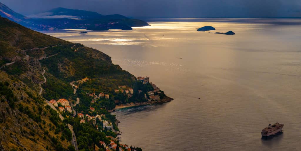 View of Dubrovnik harbor from Mt. Srdj with a winding road, beautiful villas, and a cruise ship.
