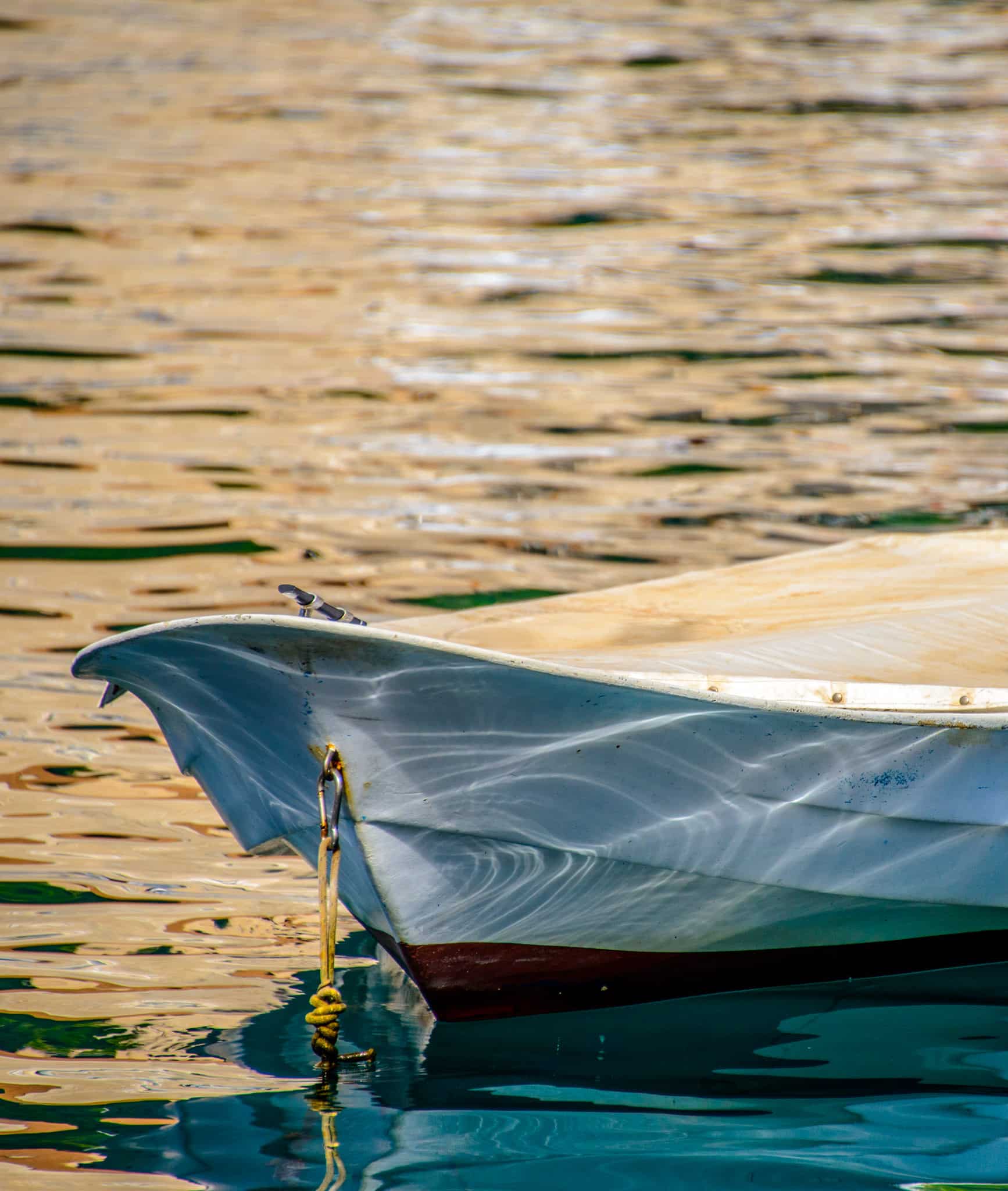 Sunlight reflecting off the water in the harbor of Dubrovnik Old Town adorns the bow of a moored rowboat.