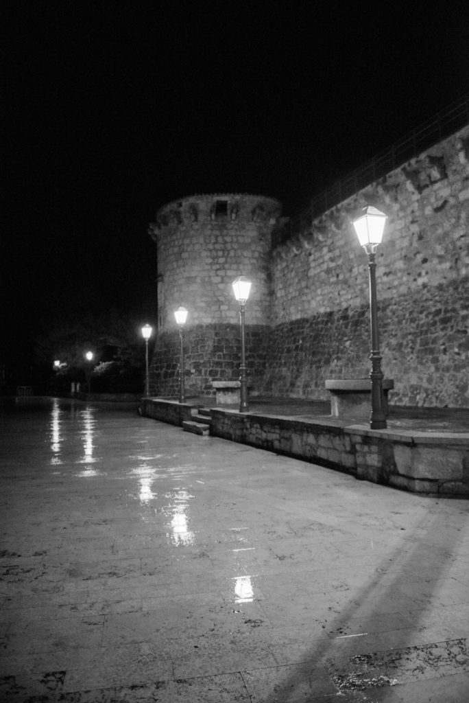 Street lights reflect in wet marble pavers along a wall of the Francopan Castle in Krk on the island of Krk in Croatia.