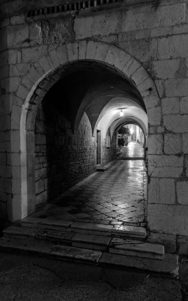 A nighttime view through a vaulted tunnel to an old cobbled street in the heart of Old Town Krk on the island of Krk in Croatia.