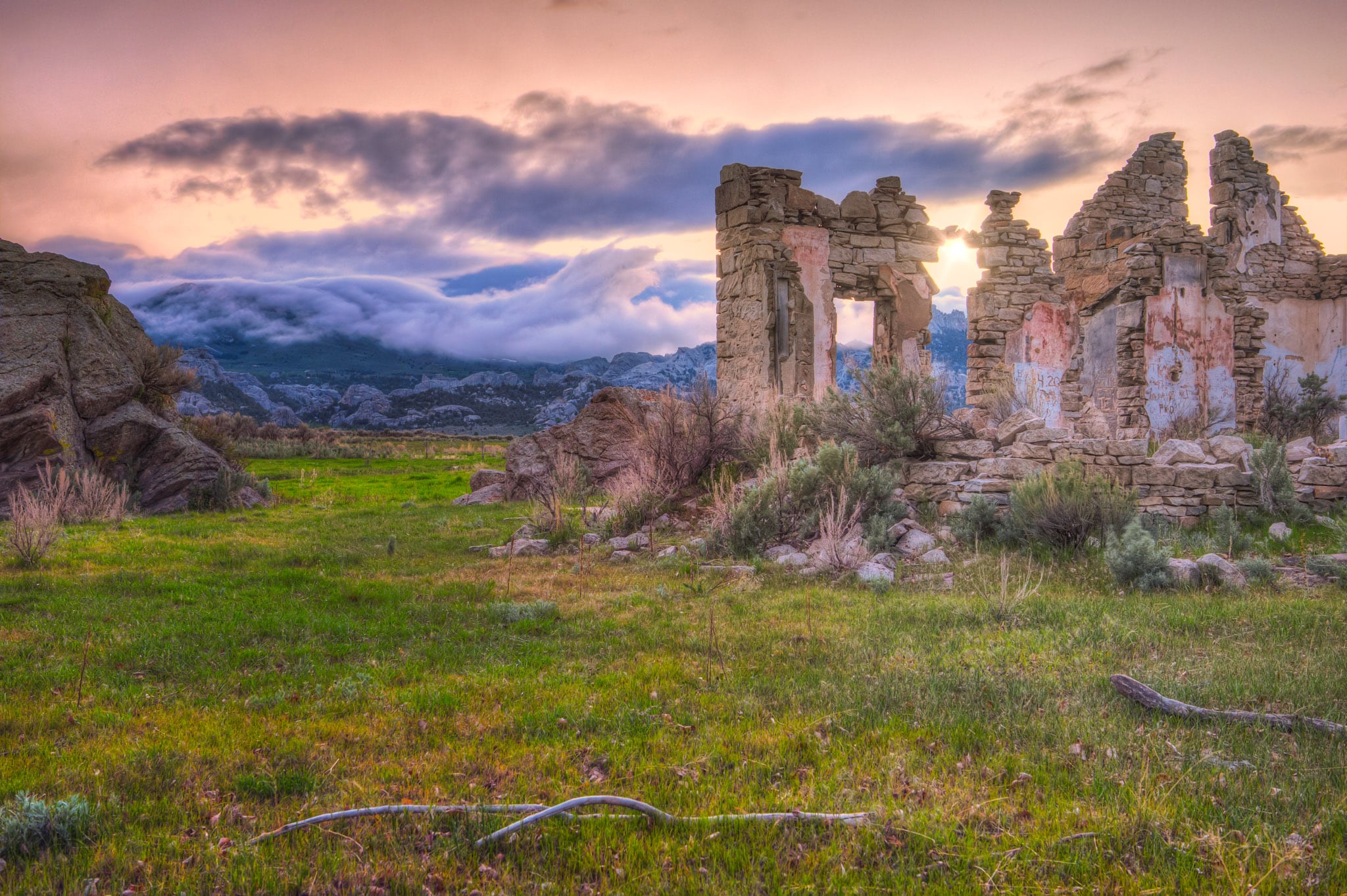 Clouds roll down the Albion Mountains at sunet with stone ruins in the foreground in City of Rocks National Reserve in Idaho.