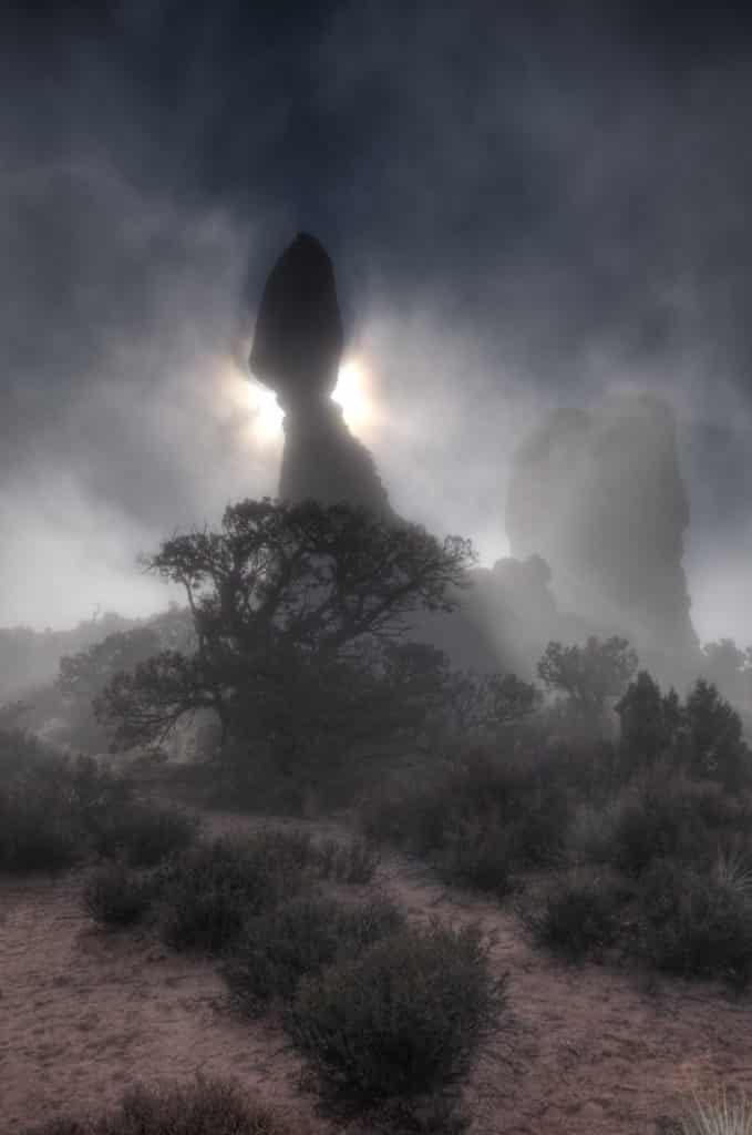 Balanced Rock backlit by the sun on a foggy morning in Arches National Park.