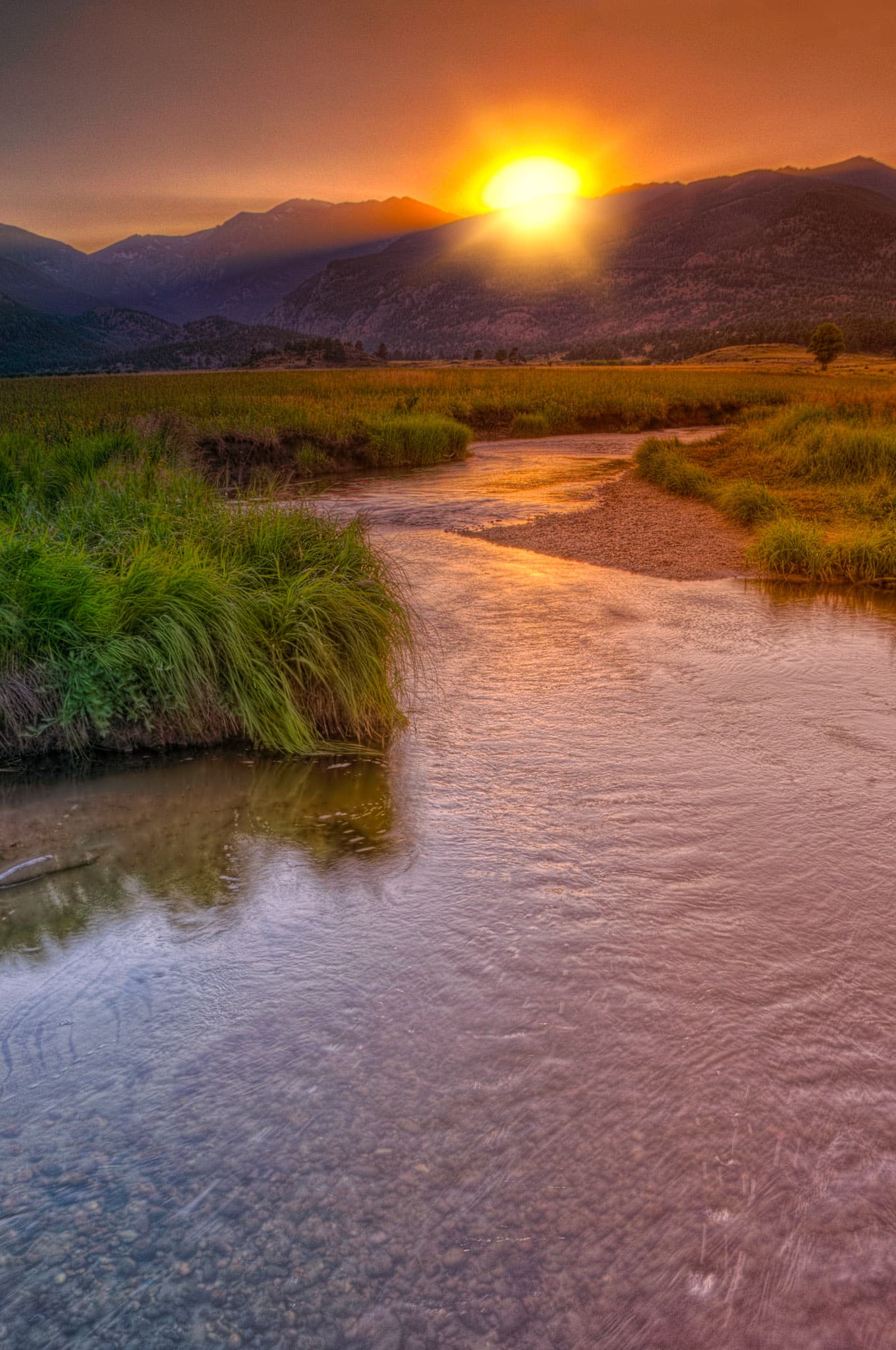 The sun dips behind Beaver Mountain as seen from the edge of Big Thompson River as it meanders through Moraine Park in Rocky Mountain National Park.