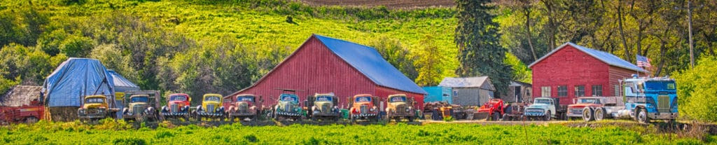 A row of mostly older trucks and other farm machinery are all lined up in front of a farm in eastern Washington near Colfax.