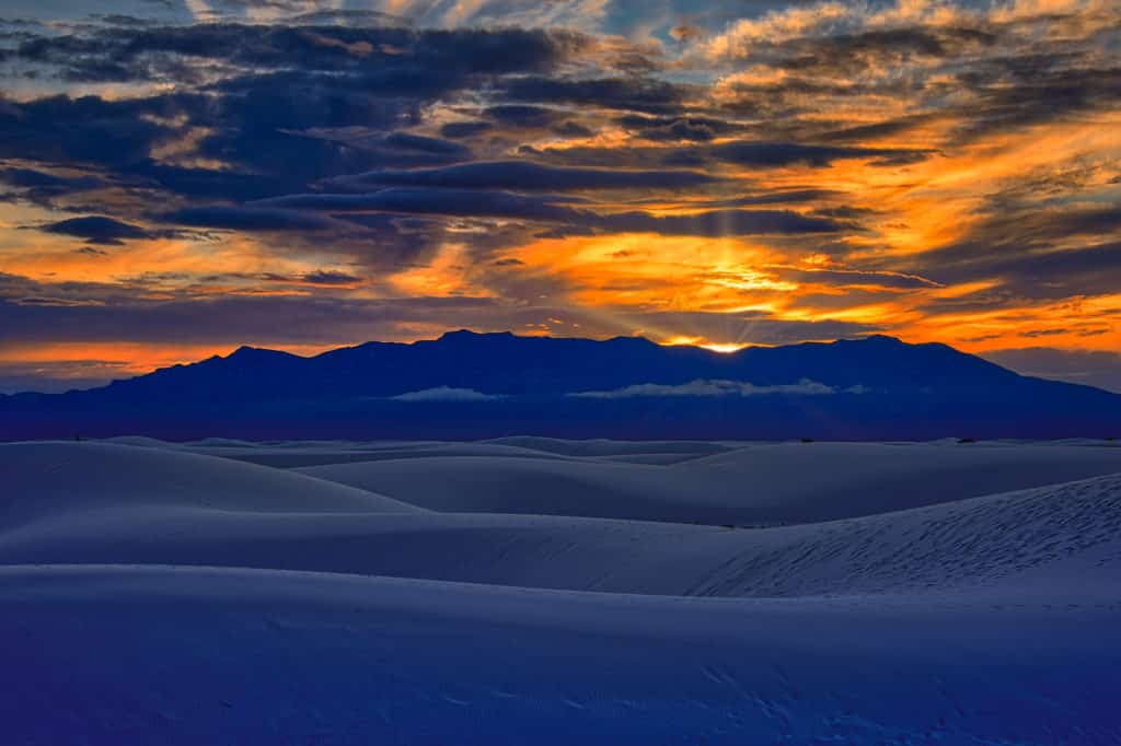 The setting sun turns the skies above the San Andres Mountains yellow, orange, and red; and, give the gypsum sands a blue tint. This photograph was taken from the Alkali Flat Trail in White Sands National Monument near Alamogordo, New Mexico.