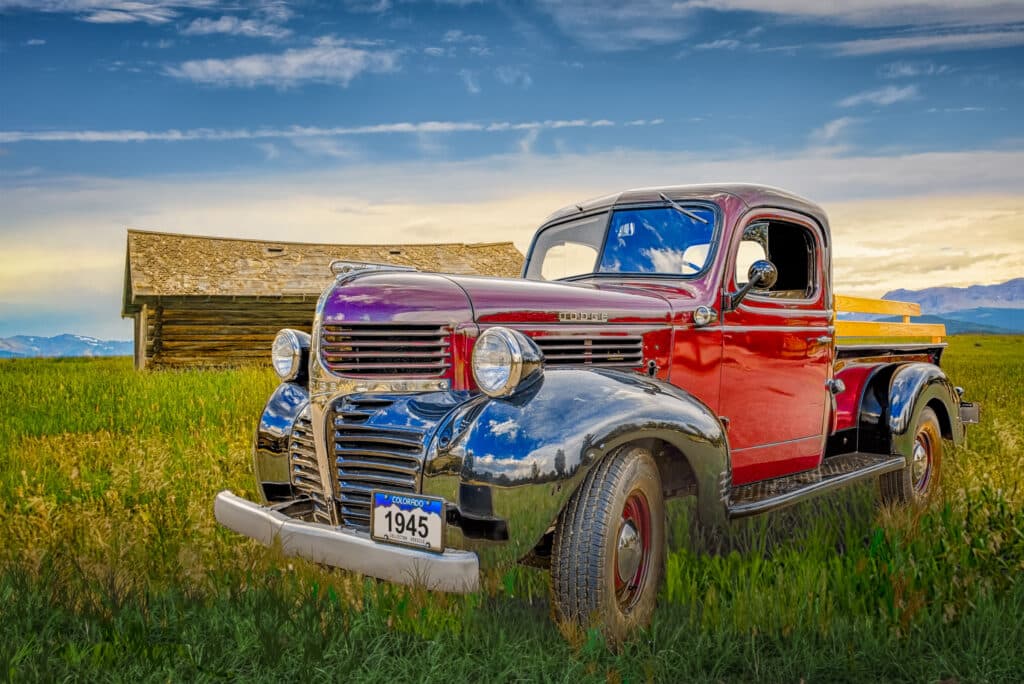 1945 Dodge Pickup Truck with red body and black fenders, in a field with a log cabin in the distance.