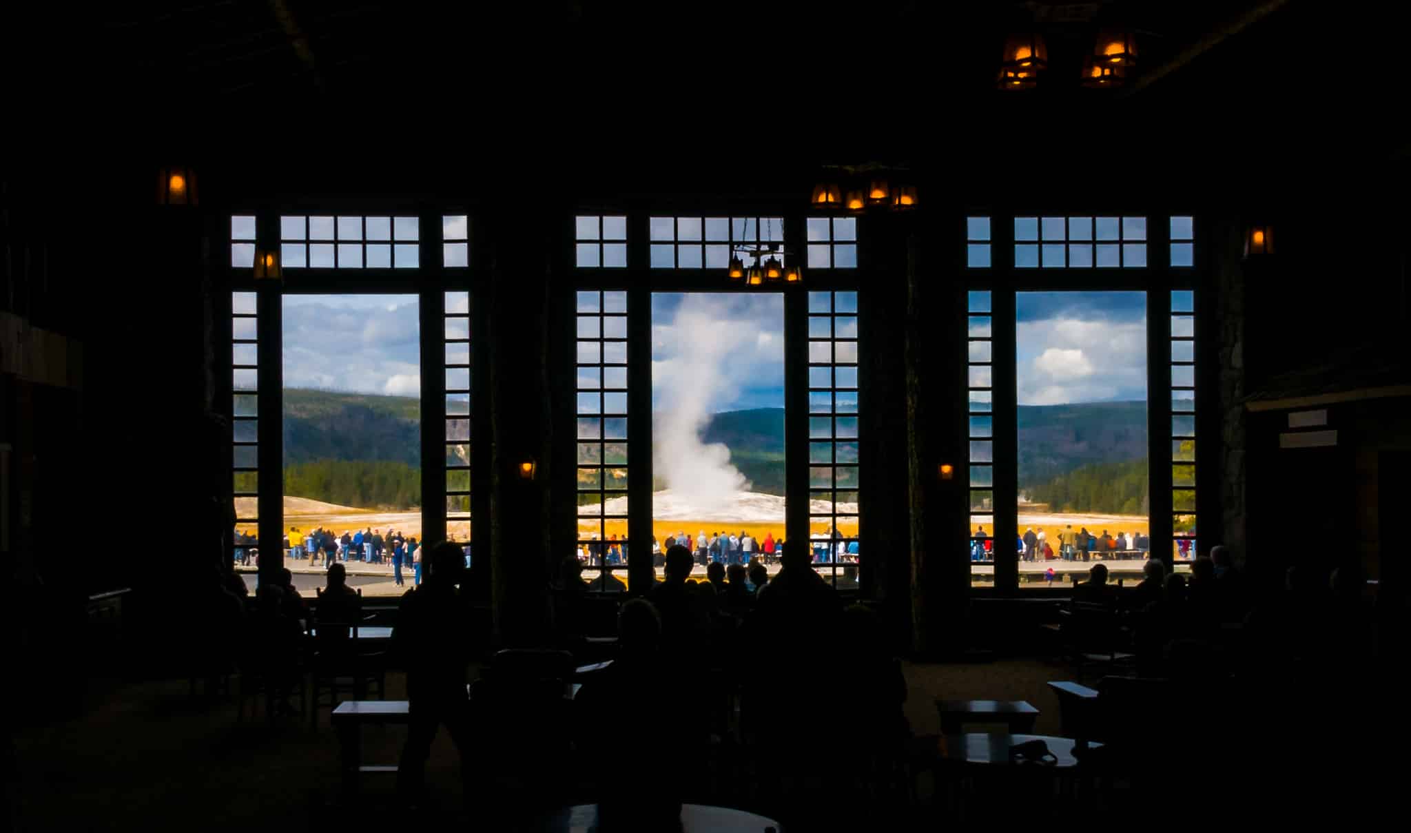 Visitors inside and outside the Old Faithful Lodge watch Old Faithful erupt.