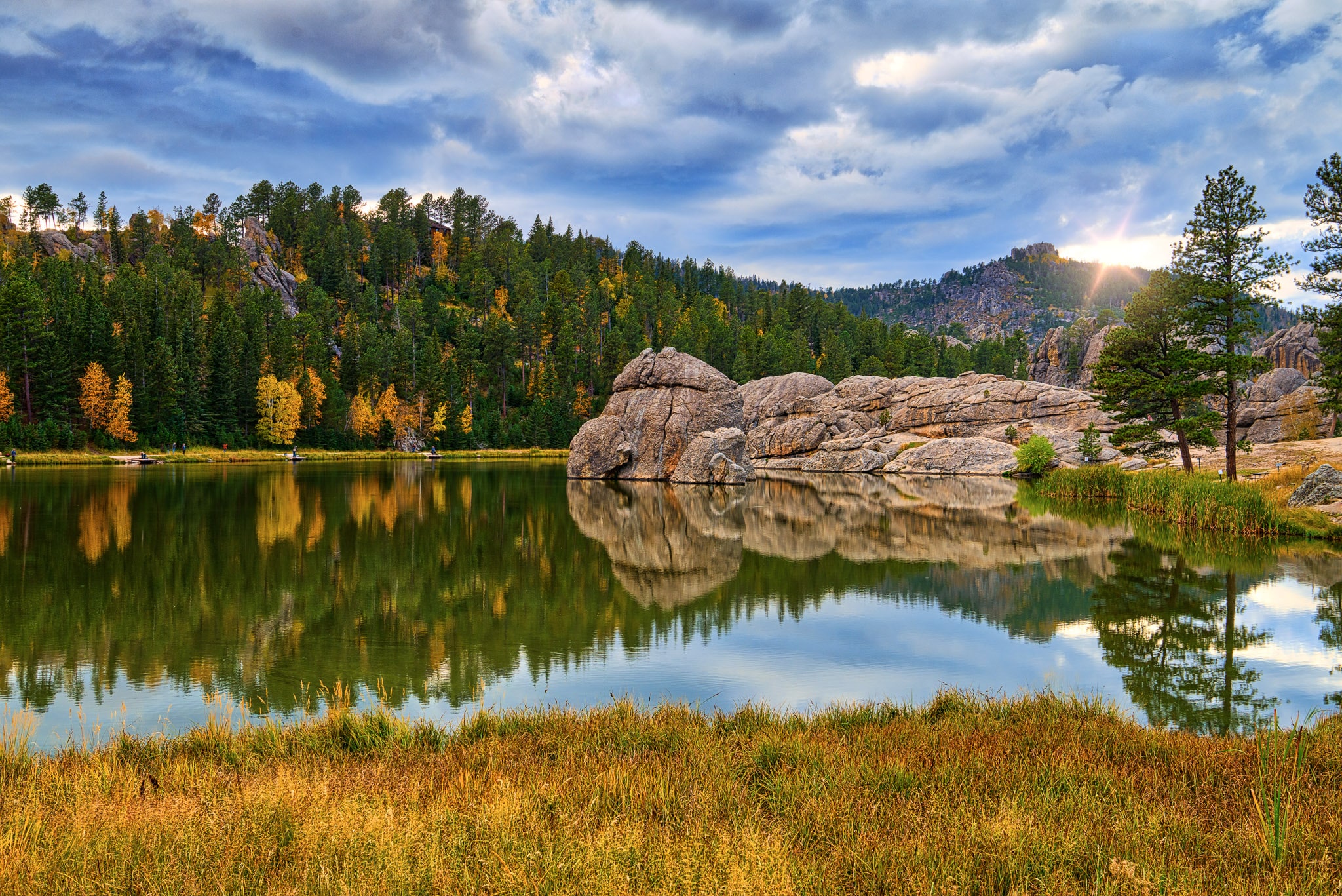 Clouds almost obscure the afternoon autumn sun as it highlights a granite rock formation and causes the multi-colored foliage to reflect in the still waters of Sylvan Lake in Custer State Park in South Dakota. Part of the Black Hills Landscapes article.