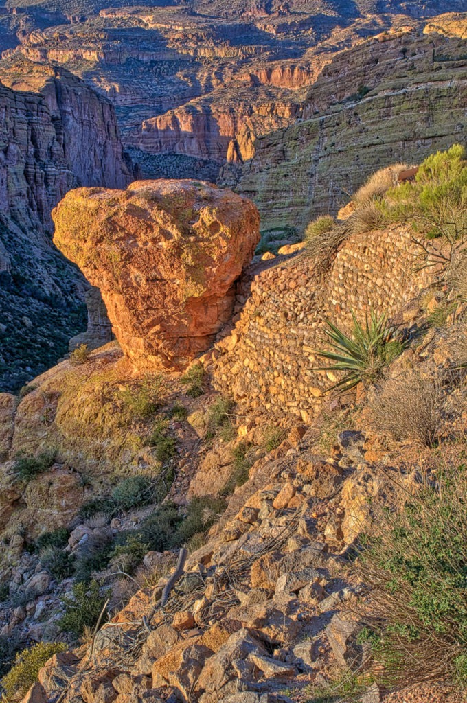 A view along the side of the Apache Trail showing a lone rock balanced upon a cliff, along with some erosion mitigation.