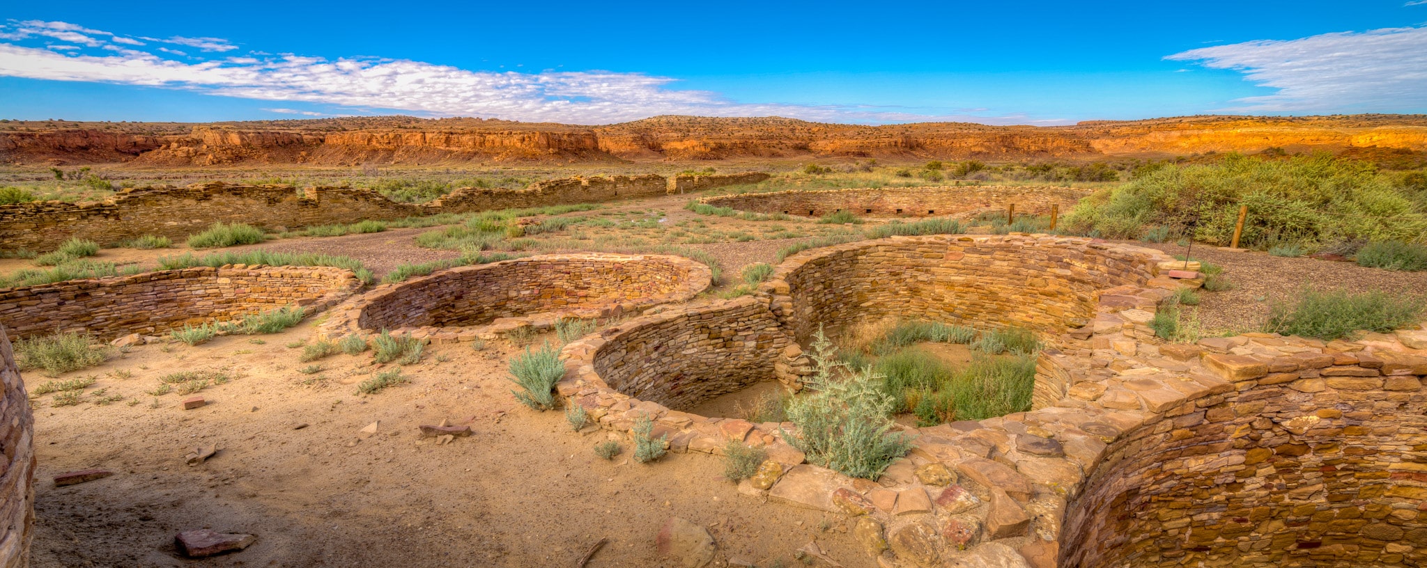 This panoramic view shows a cluster of kivas located in the northeast corner of Chetro Ketl's courtyard in Chaco Canyon, New Mexico. The large kiva in the distance is one of two great kivas at Chetro Ketl.
