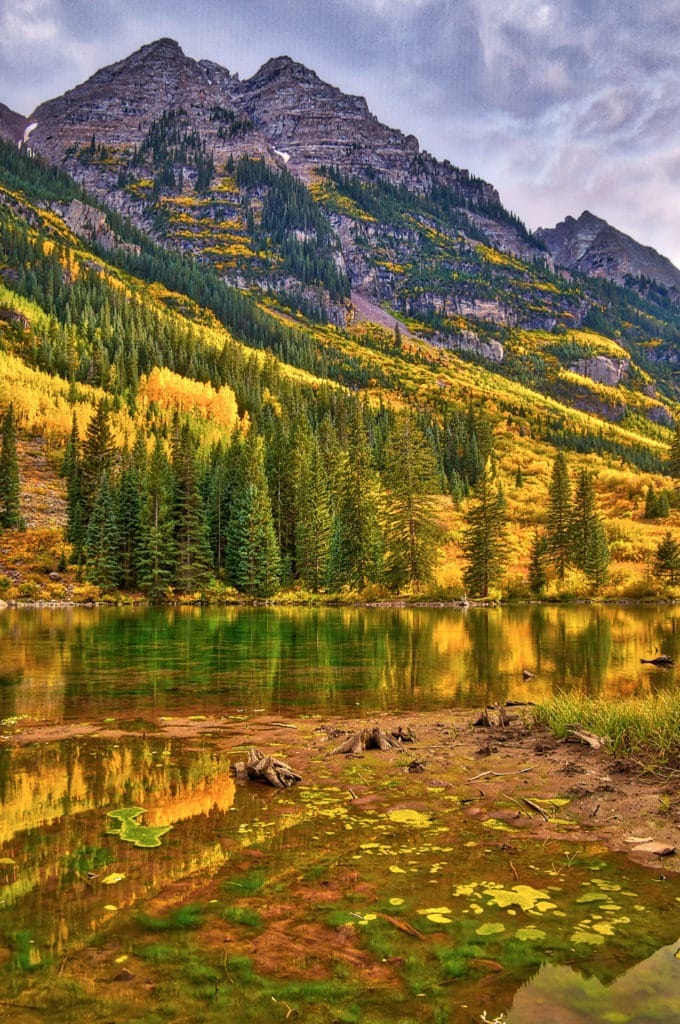 A typical fall afternoon in the Maroon Bells Recreations Area near Aspen, Colorado. The sun peeks through the gray clouds to illuminate the beautiful gold aspens.