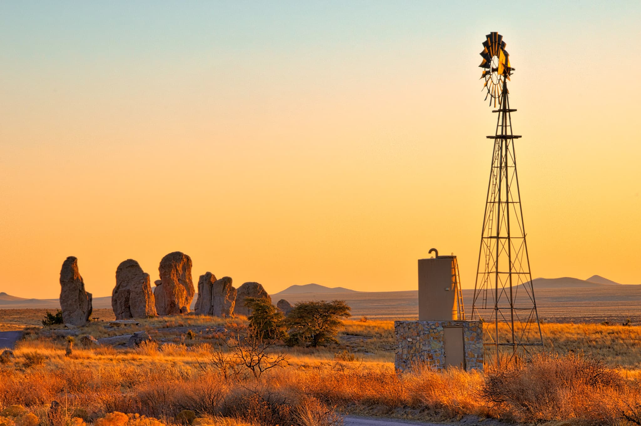 A windmill and water tank stand on the edge of City of Rocks at sunset.