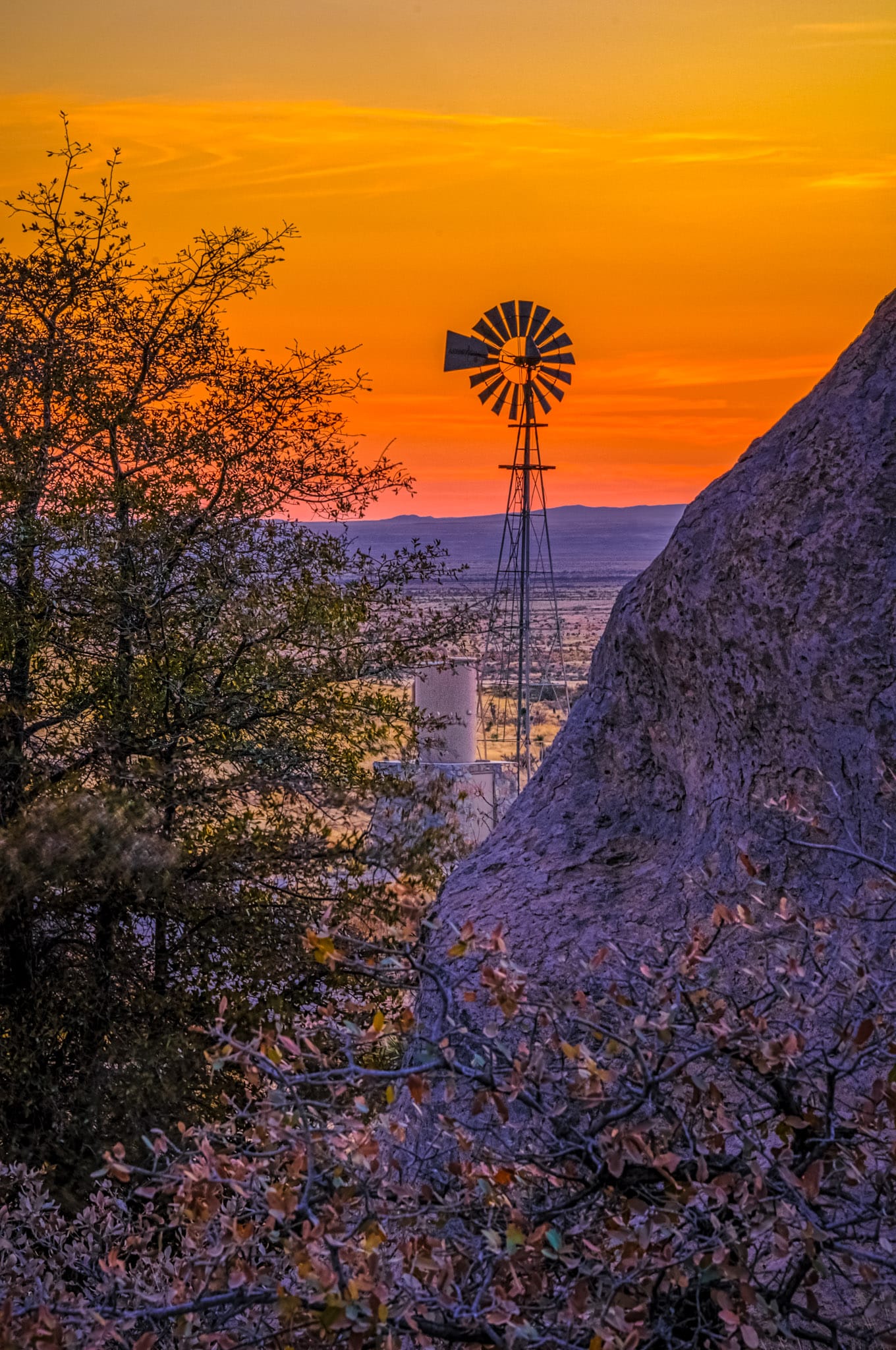 A windmill and water tank stand on the edge of City of Rocks at sunset.