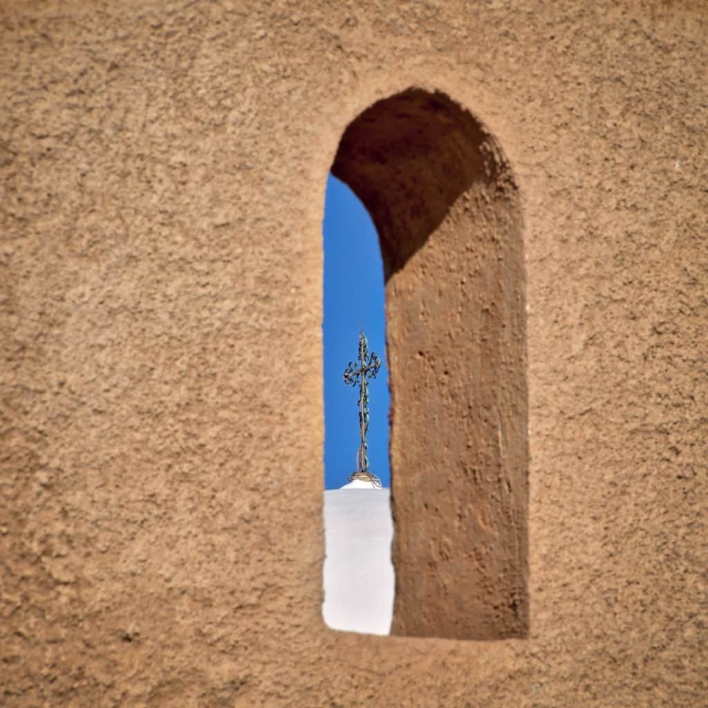 The wrought iron cross atop the basilica of San Xavier del Bac is seen through an opening in the outer stucco wall of the church compound located south of Tucson, Arizona.