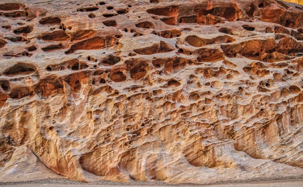 These pock marks in the Wingate Sandstone are due to differential erosion of poorly cemented sand. This view is from along Capitol Gorge Road in Capitol Reef National Park, Utah.
