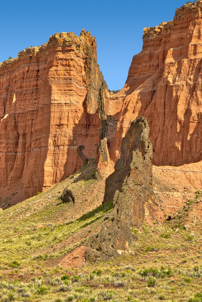 The vertical igneous intrusion, called a dike, forced its way through the Entrada Sandstone long after the Entrada was deposited. Slowly, wind, rain, and freezing water have eroded the crumbly Entrada, revealing these fins of igneous rock. This dike can be seen in the Upper Cathedral Valley along Cathedral Road in Capitol Reef National Park, Utah.