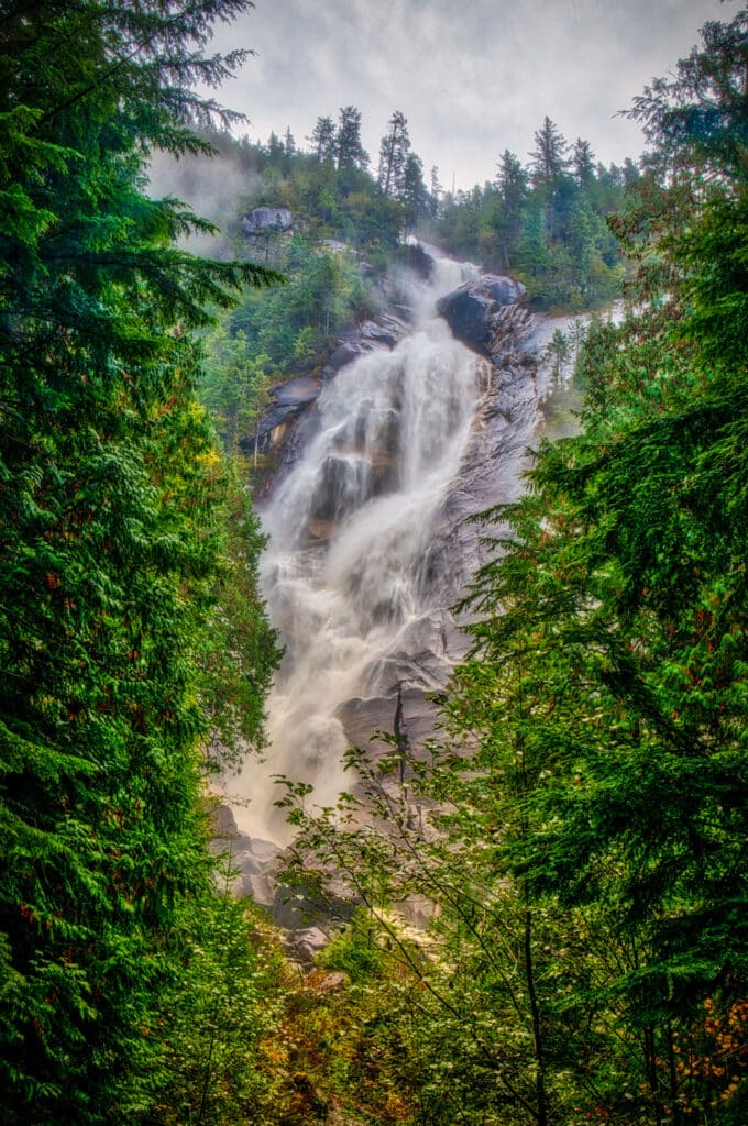 A view of Shannon Falls through a frame of pine trees in Shannon Falls Provincial Park off the Sea-to-sky Highway along the coast of British Columbia.