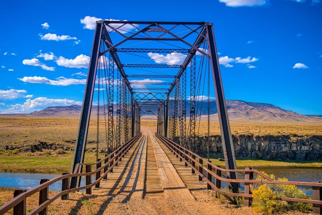 This is a view through the Lobato Bridge (Costillo Crossing Bridge) on the Rio Grande River, about 13 miles east of Antonito, Colorado, on Conejos County Road G. The Lobato Bridge is the southernmost bridge across the Rio Grande River in Colorado. This bridge is classified as a two-span Thacher through truss bridge.