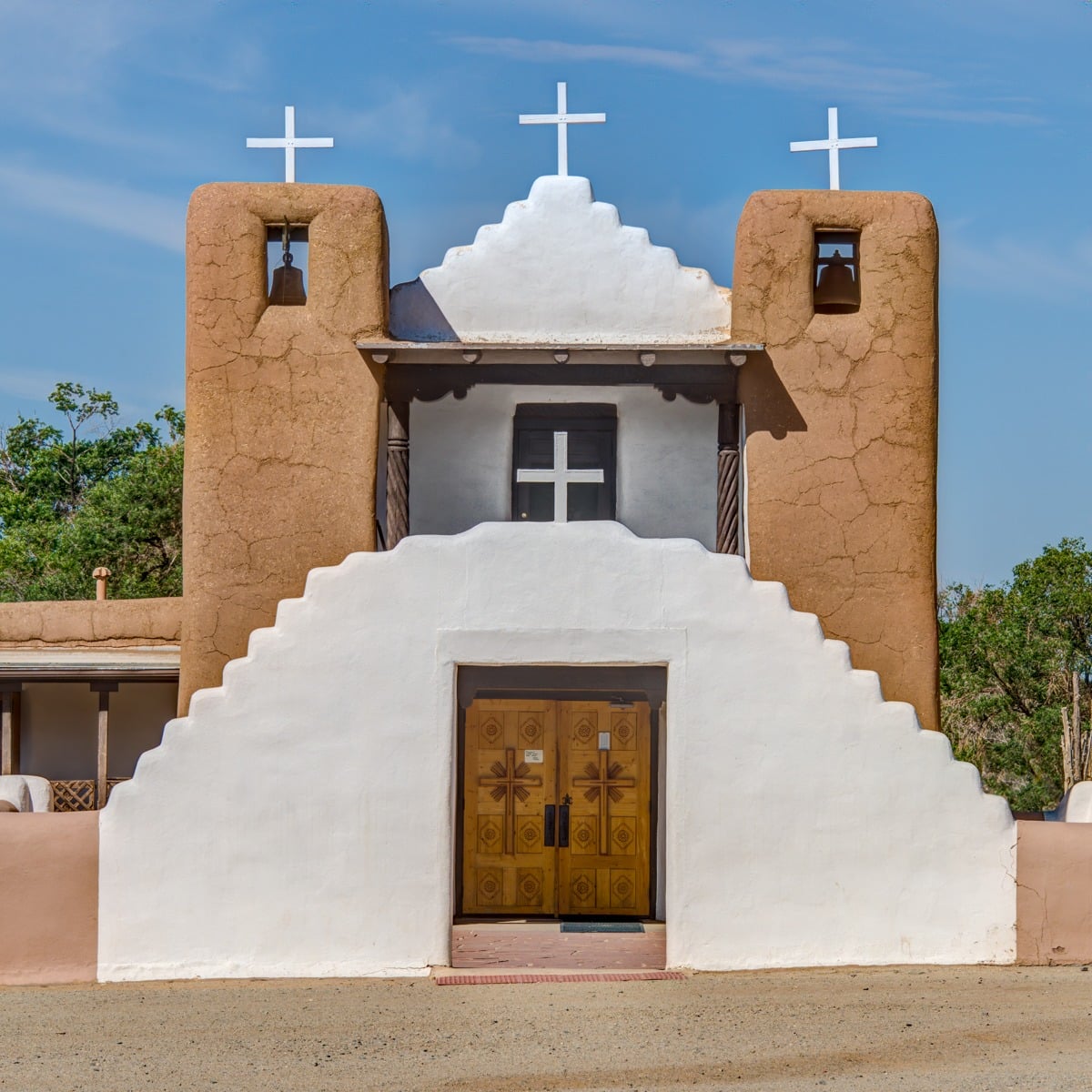 A frontal view of St. Jerome (San Geronimo) Catholic Chapel with the whitewashed arched gateway in front. The chapel is located in the heart of Taos Pueblo, New Mexico.