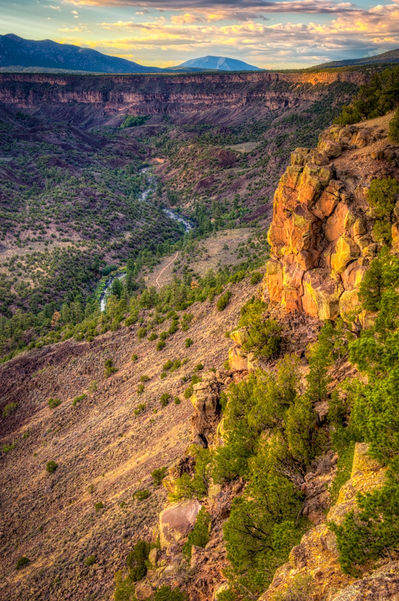 The cliffs and hills along the Rio Grande gorge in Wild Rivers Recreation Area are tinged orange and yellow by the late afternoon sun.