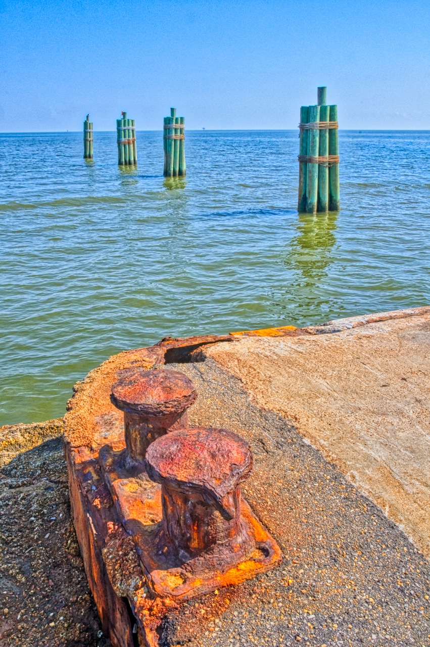 A rusty pier and green pilings lead you eye out to several drilling platforms in the Gulf of Mexico, near Fort Morgan, Alabama