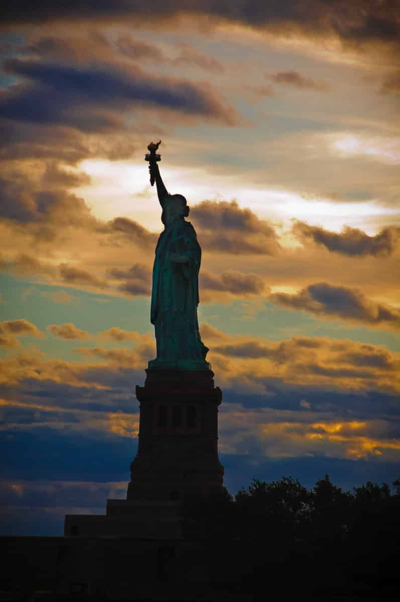 The Statue of Liberty is silhouetted against the evening sky in the Upper Bay of New York City.
