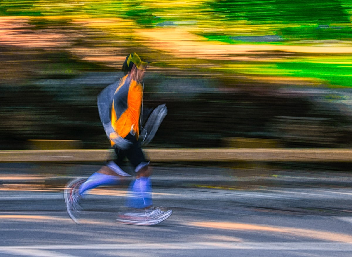A panning shot creates and abstract image of a jogger running in Central Park, New York.
