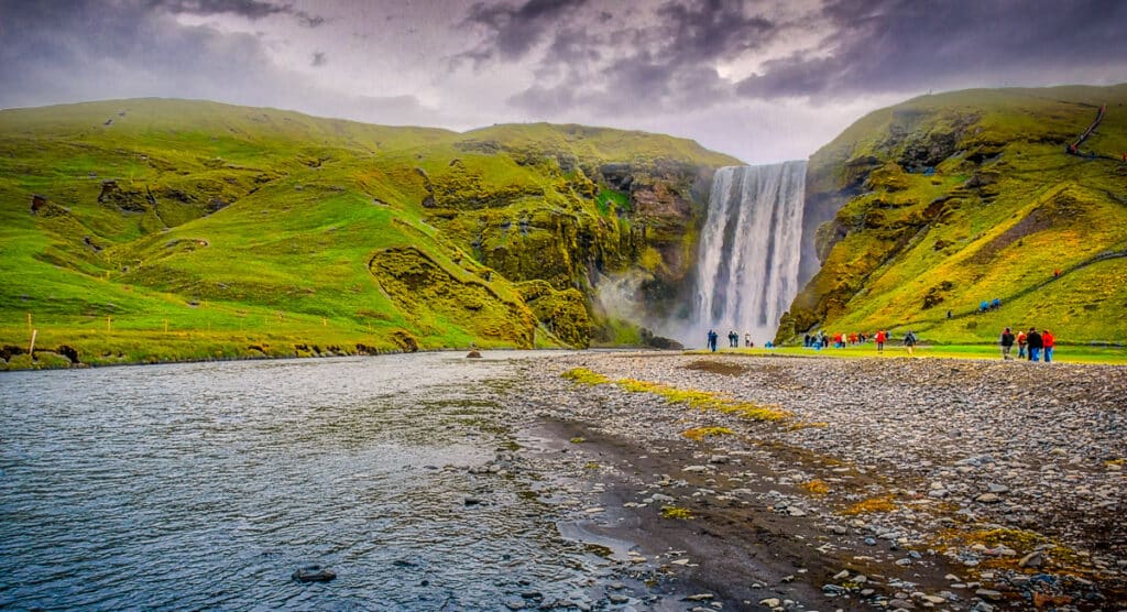This is a wide view of Skógafoss, showing both the top of the falls and the base, where the plunging water creates billows of mist. Skógafoss is a waterfall in southern Iceland, along Route 1. It's source is runoff from the glacier Eyjafjallajökull and the glacier Myrdalsjokull.