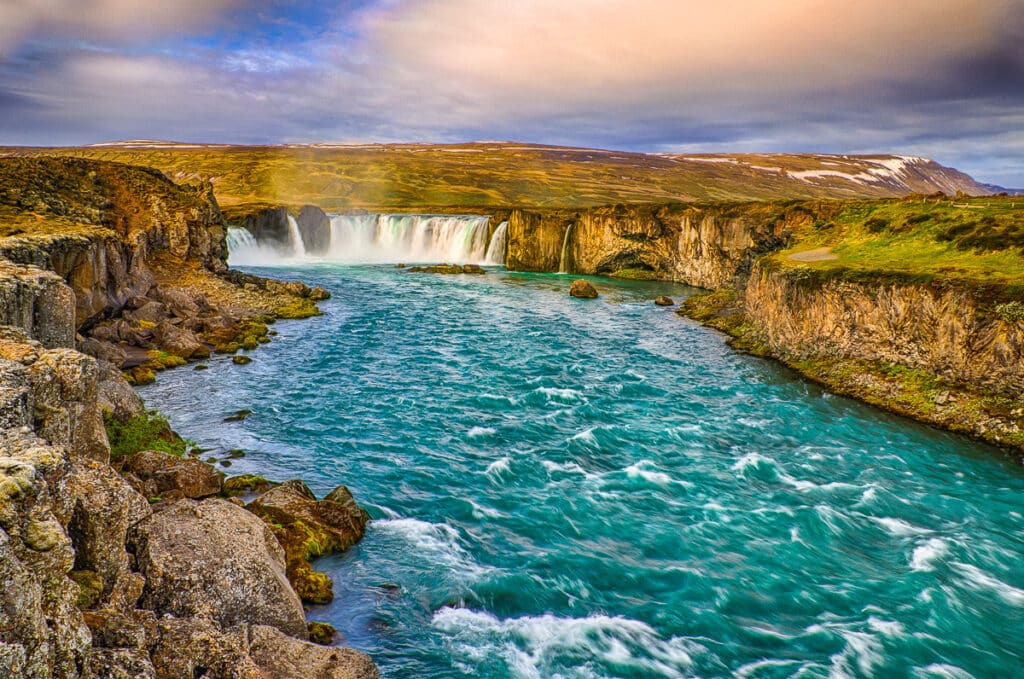 Goðafoss is a broad, but shallow, waterfall that cascades over a bench of lava within the river Skjálfandafljót. Goðafoss translates as Waterfall of the Gods. And for good reason. About 1000 AD, the Alþingi (Icelandic parliament) voted to convert to Christianity. On his way home, Þorgeir Ljósvetningagoði, the country´s Lawspeaker (like Attorney General or Justice Minister), threw his idols of Norse gods into the river Skjálfandafljót at these falls.