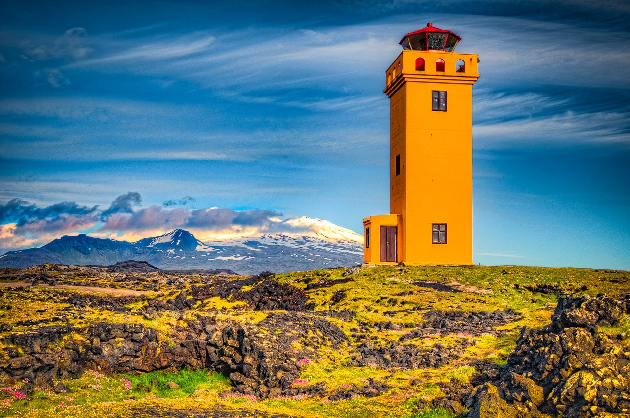 Lighthouse along the Svörtuloft cliffs at the western tip of the Snæfellsnes peninsula in Iceland. In the background is snowcapped peak of Snæfellsjökull National Park. If you are on land, it is called Skálasnagaviti. If you are out at sea, it is called Svörtuloftaviti.