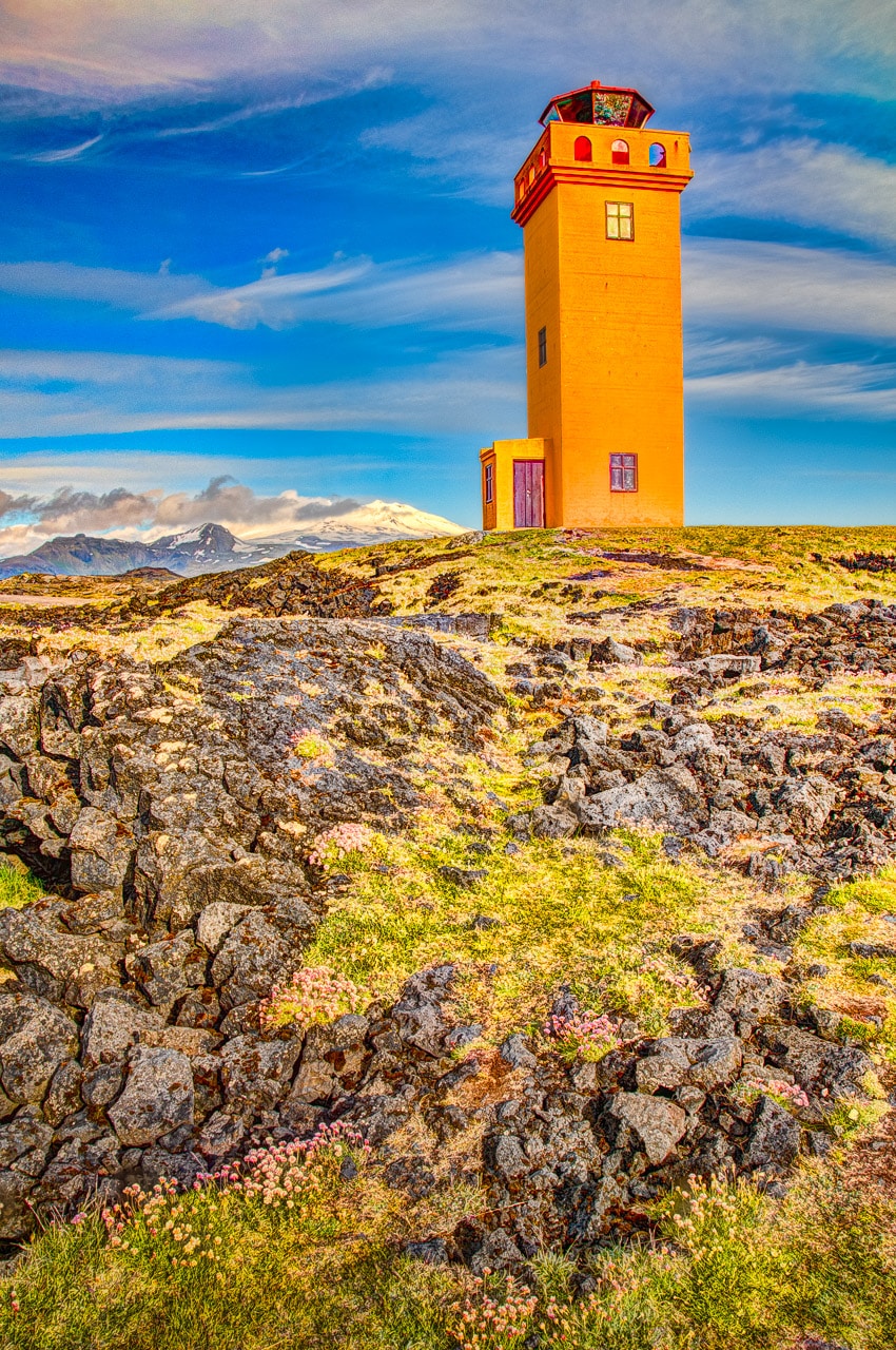 Lighthouse along the Svörtuloft cliffs at the western tip of the Snæfellsnes peninsula in Iceland. In the background is snowcapped peak of Snæfellsjökull National Park.