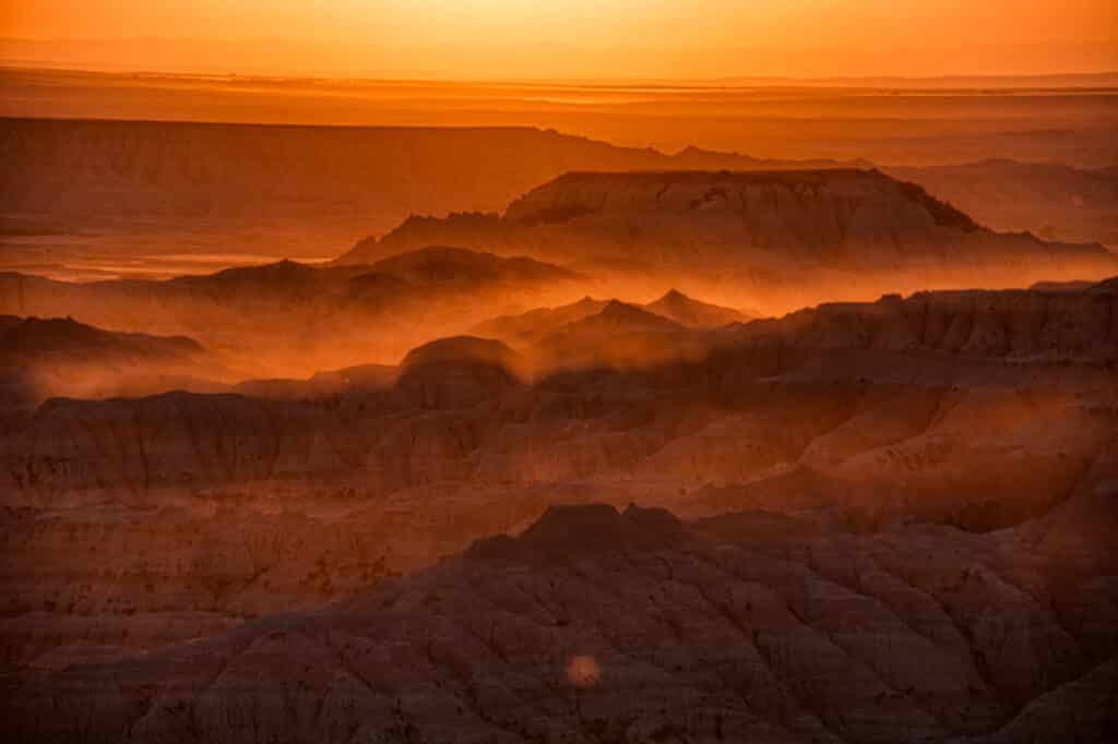 Dust catches the rays of the setting sun in this westward view across the eroded landscape of Badlands National Park in South Dakota.