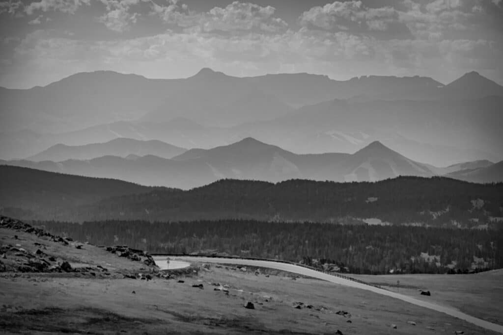 Black and white view of switchbacks with several ridges of hills and mountains in the distance.